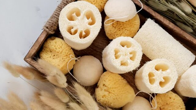 Zero waste hygiene products. Loofah sponges, konnyaku sponges in a wooden tray and dried flowers on a light shabby background.Hygiene and beauty natural eco-friendly products