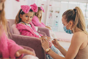 Little girls having part in spa center. Kids are holding a drink glass. Focus is on toddler girl.