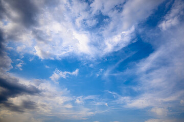 Stormy grey cloud with puffy white ones and blue sky. Horizontal cloudscape shot near horizon.