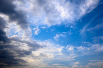 Stormy grey cloud with puffy white ones and blue sky. Horizontal cloudscape shot near horizon.