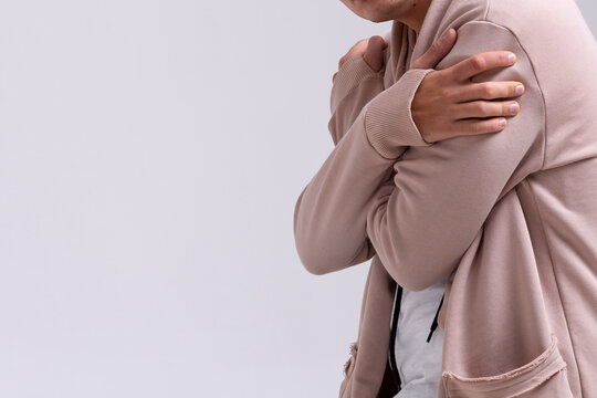 a man dressed in a white monk's robe stands with his arms crossed on his chest expressing the emotions of fear of closeness and anxiety on a gray background copy space close-up