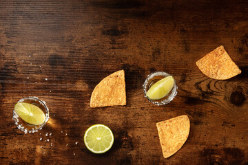 Tequila shots with salty rims, lime slices, and nacho chips,
