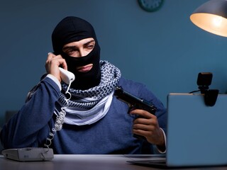 Terrorist burglar with gun working at computer