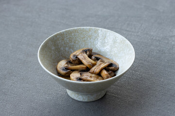Sautéed white mushrooms in oyster sauce in a ceramic bowl isolated on a gray background.