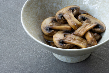 Closeup of sautéed white mushrooms in oyster sauce in a ceramic bowl on a gray background.