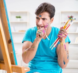 Young funny artist working on new painting in his studio