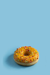 Obraz na płótnie Canvas Bright donut with yellow glaze and a multi-colored sprinkle on blue vertical background .Sweet minimalist food image.