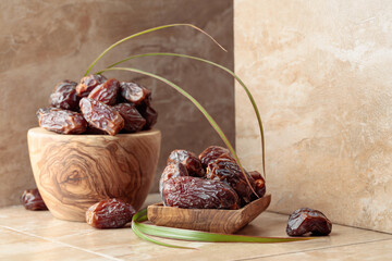 Dates fruit in a wooden dish on a beige ceramic table.