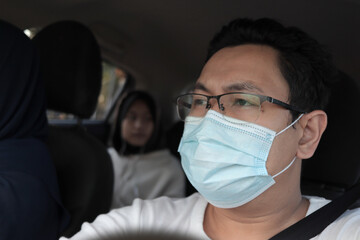Asian male driver wearing facial protective mask while driving his car, private transportation during coronavirus covid19 pandemic