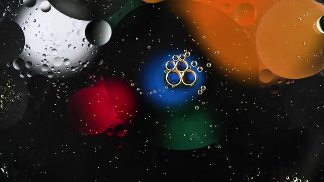 Multi-colored drops of oil floating on the water create a cosmic abstraction.