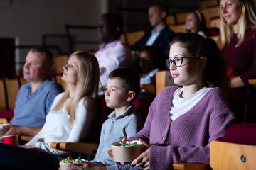 Portrait of teen girl with family sitting in movie theater with popcorn and drinks, watching interesting film