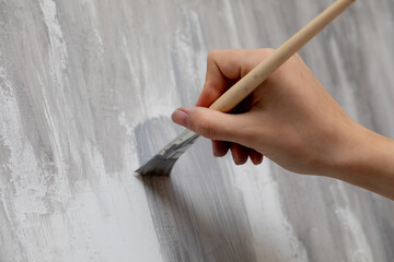 Abstract monochrome grey background, pattern in fancy design. Closeup of texture in white, gray and black brush strokes of acrylic paint. woman hand holds a brush covered by grey acrylic paint.