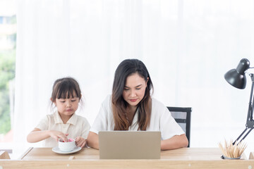  Asian young mother use computer notebook with little daughter sitting beside her at home