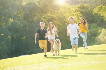 Group of happy children playing on green grass in a spring park with a dog. High quality photo.