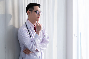 Young male doctor standing in his office. Professional doctor stands up in his room office in hospital building. Young male doctor standing, wearing stethoscope and lab coat.