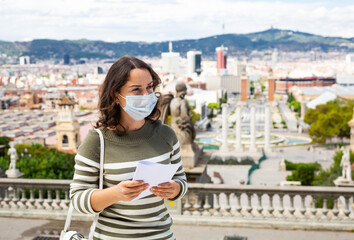 Young woman tourist in medical mask holding paper map in the city center of Barcelona