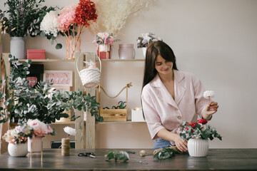 Young woman florist working in her flower studio, making beautiful bouquet using fresh plants and flowers.