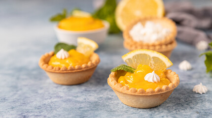 Mini tarts with lemon curd, mini meringue, lemon slices and mint on blue concrete background.
