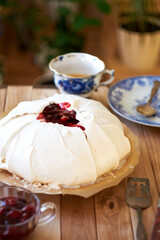 Pavlova cake with vanilla cream and cherry sauce. Side view. Wooden background and green plants.
