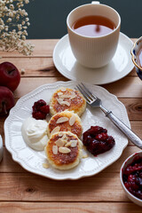 Cottage cheese pancakes with almond petals, sour cream and a cup of tea. Side view. Syrnik