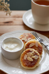 Cottage cheese pancakes with almond petals, sour cream and a cup of tea. Side view. Syrnik