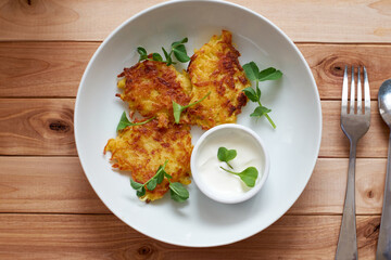 Potato pancakes or pancakes with sour cream in a plate on a wooden background. Top view.