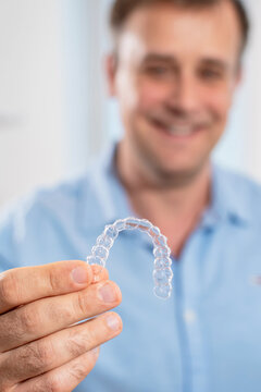 Smiling orthodontist doctor holds transparent aligners in his hands