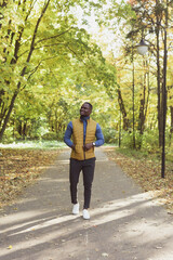 Cheerful african american young man in stylish clothes walks in autumn park on sunny warm autumn day. Concept of weekend and outdoor recreation