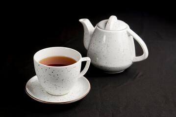 White tea cup with tea pot over black background.