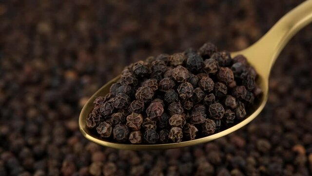 peppercorn in golden spoon and on black background. Flavorful and aromatic black pepper. 4K UHD video