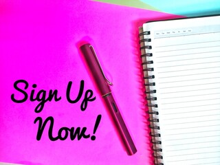 Sign Up Now! Written on a pink paper with a note book and a pen.