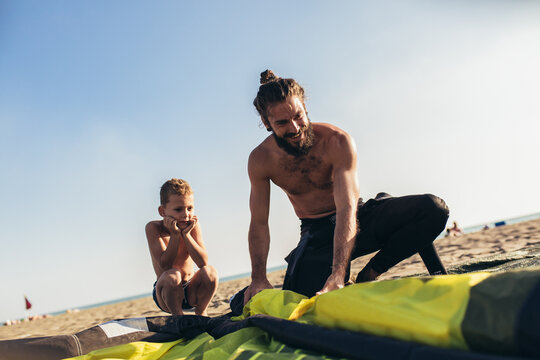 Father and son in wetsuits with kite equipment for surfing