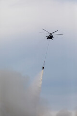 Firefighter helicopter with a water tank in smoke from a fire. Swirling smoke from a large fire.