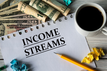 INCOME STREAMS - words on a white sheet against a background of banknotes, cups of coffee and pencil