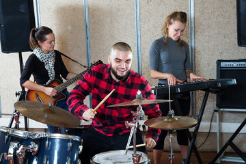 Music garage band with expressive male drummer rehearsing in recording music studio