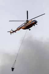 Firefighter helicopter with a water tank in smoke from a fire. Swirling smoke from a large fire.