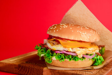 Bacon and beef patty burger with red onions and cheese over red background. Fast food, junk food concept.