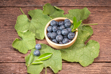 Fresh Blueberries on wooden tray with green leaves background.