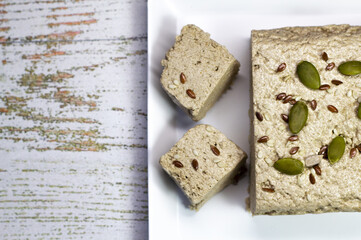 Halva close-up on a white plate on a white wooden background. Traditional oriental dessert sweet halva. Halva made from sunflower seeds. top view, flat lay, copyspace.