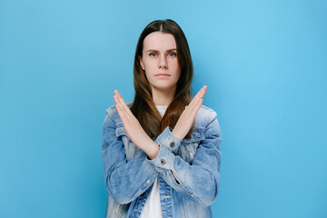 Portrait of young millennial woman making stop sign with crossed hands, serious girl 20s denying,...