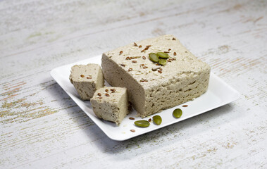 Halva close-up on a white plate on a white wooden background. Traditional oriental dessert sweet halva. Halva made from sunflower seeds. Top view, copyspace.