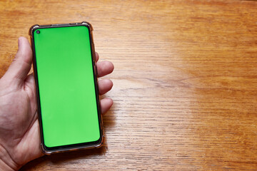 Male hand holds a phone with a green screen on a desktop background.