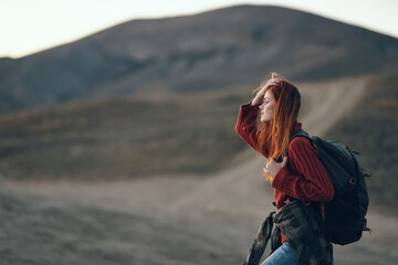 a traveler in a sweater with a backpack on her back looks to the side outdoors in the mountains