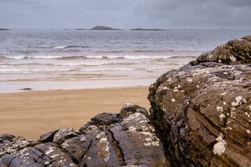 Rough stone and sandy beach and small islands in Atlantic ocean, West coast of Ireland. Cloudy sky. Irish nature background