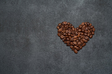 Heart shaped roasted coffee beans on dark concrete background