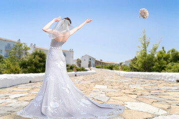 Fototapeta na wymiar 晴天の空に向かってブーケトスをする純白のウエディングドレスを着た花嫁