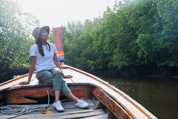 Portrait image of a beautiful young asian woman sitting on a long tail boat while traveling the mangrove forest