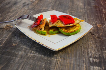 Ready-made dish of fried zucchini, pepper and chicken with spices on a white plate with a gold border