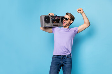 Portrait of carefree person hold boom box on shoulder fist up open mouth smile isolated on blue color background