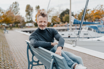 Obraz premium Laid-back man relaxing on a bench at the waterfront at the marina